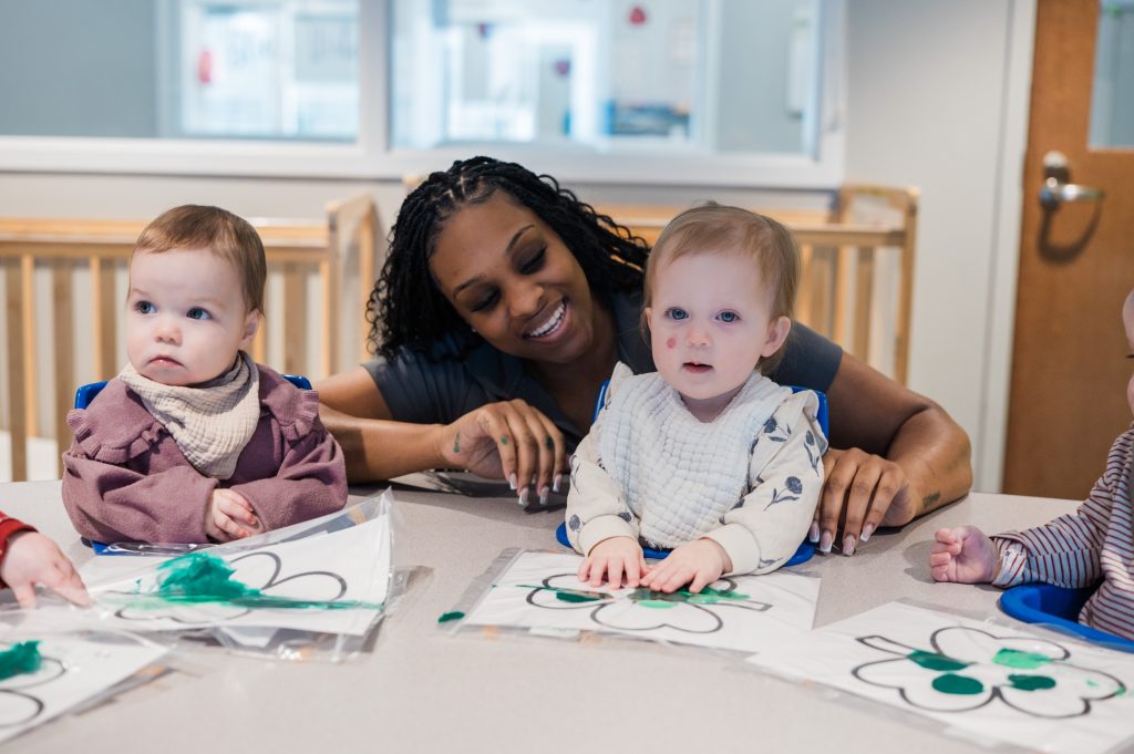 Teacher joyfully engaging with infant during a painting activity at Ardent Preschool & Daycare, fostering creativity and connection.